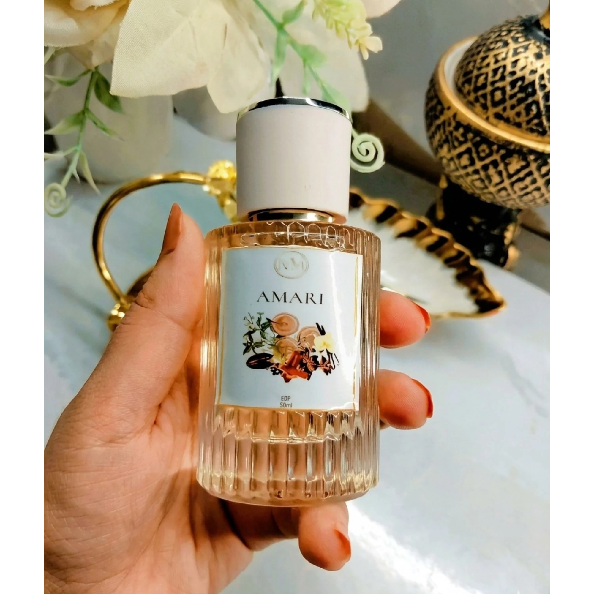 Hand holding a perfume bottle labeled 'Amari' with decorative background